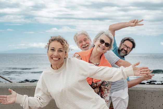 Gelukkige, speelse familiegroep van meerdere generaties in de open lucht aan de kust die hun vreugde uitdrukken door gebaren te maken