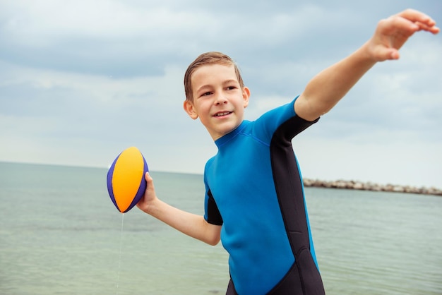 Foto gelukkige speelse jongen die met een rugbybal in de zee speelt