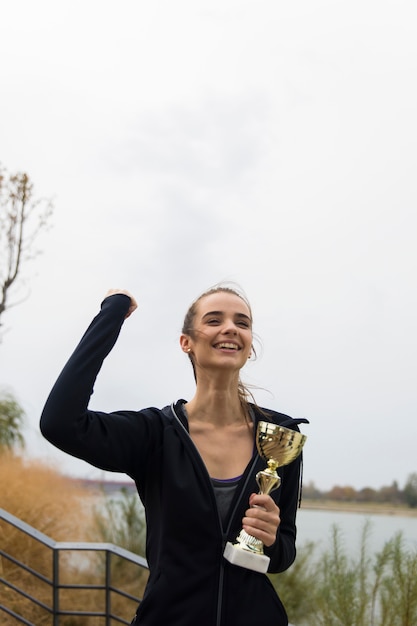 Gelukkige sportieve jonge vrouw die gouden trofeekop houden