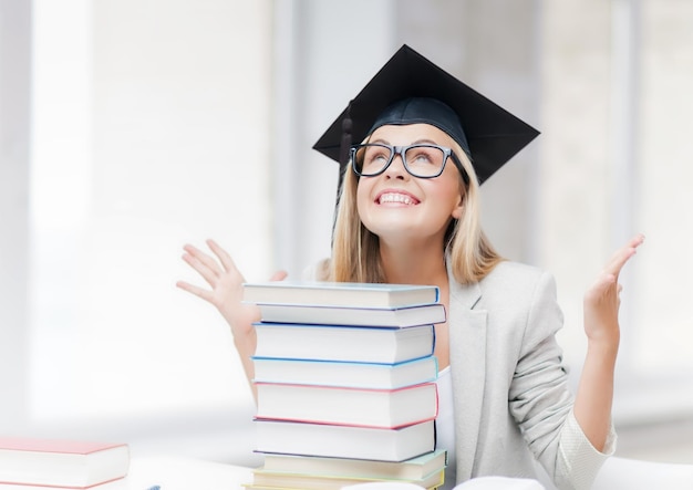 gelukkige student in afstudeerpet met stapel boeken