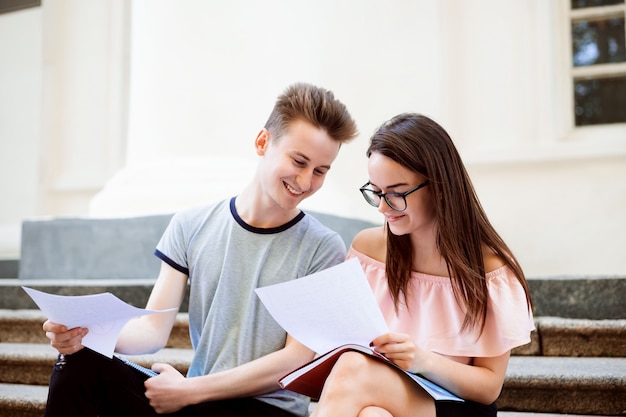 Gelukkige studenten die op de trap van de universiteit zitten en huiswerk maken