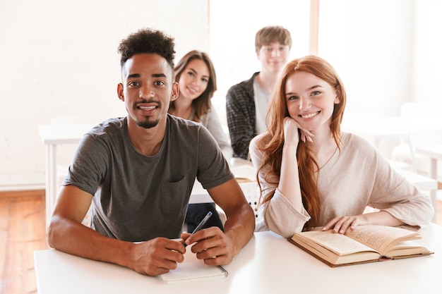 Gelukkige studenten zitten in de klas binnenshuis op zoek naar camera.