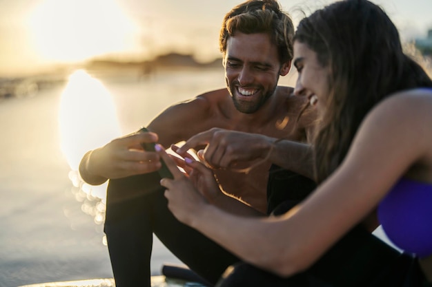 Gelukkige surfers die op een strand zitten en naar de telefoon glimlachen