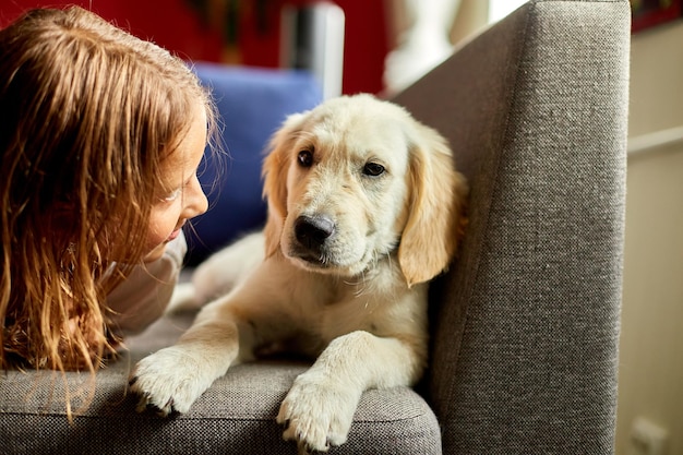 Gelukkige tiener die op bank ligt en haar puppy golden retriever omhelst