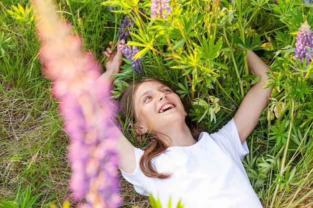 Gelukkige tiener die openlucht glimlacht. Mooie jonge tiener vrouw rusten liggend op zomer veld met bloeiende wilde bloemen groene achtergrond