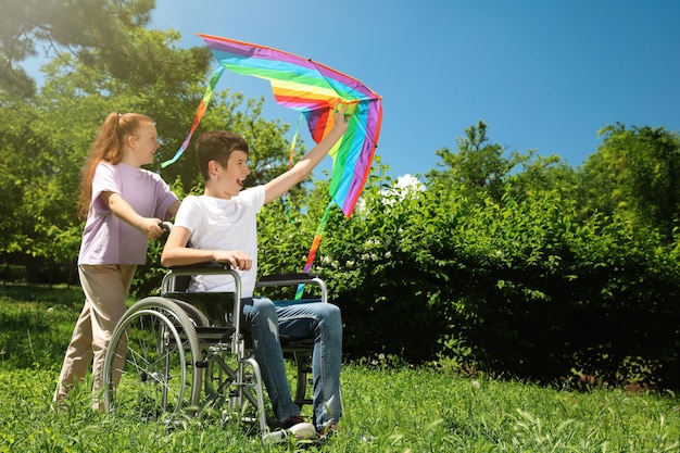 Gelukkige tiener in rolstoel met vlieger en meisje in het park op zonnige dag