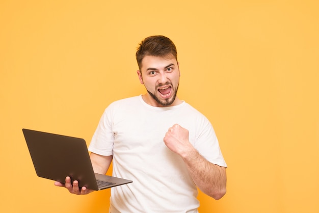 gelukkige tiener met een baard die zich op geel met laptop in zijn handen bevindt