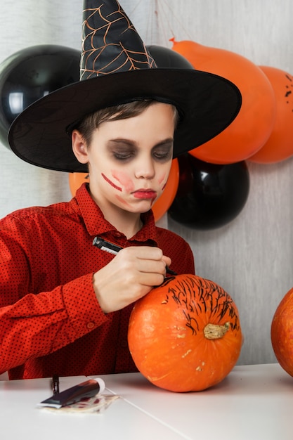 Gelukkige tienerjongen die in kostuum voor de viering van Halloween voorbereidingen treffen die een pompoen trekken