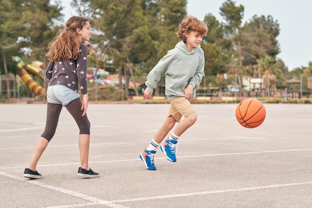 Gelukkige tienerjongen en tienermeisje spelen samen basketbal terwijl ze samen tijd doorbrengen in het zomerweekend