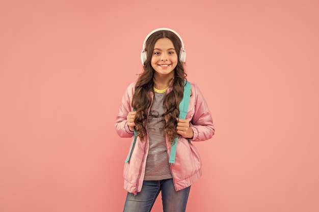 Gelukkige tienermeisje met rugzak met koptelefoon op roze achtergrond school
