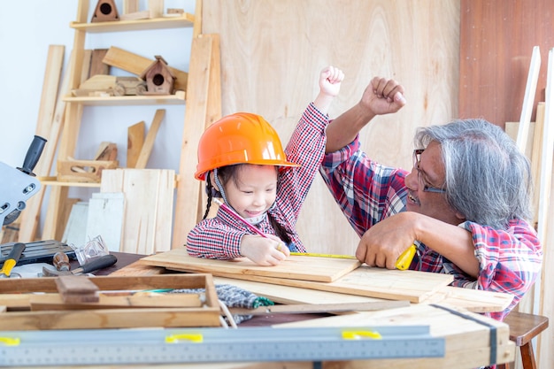 Gelukkige timmermansfamilie. Het kleine meisje en haar grootvader steken je handen op terwijl ze aan houtwerk in een houten winkel werken.