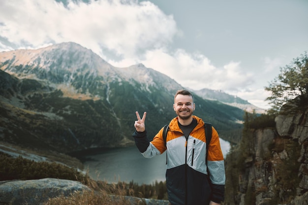 Gelukkige toerist op de top van de berg tegen een prachtig meer en bossen op de heuvels Concept van gemakkelijke wandeling tijdens het weekend Wandelaar glimlacht en kijkt naar de camera