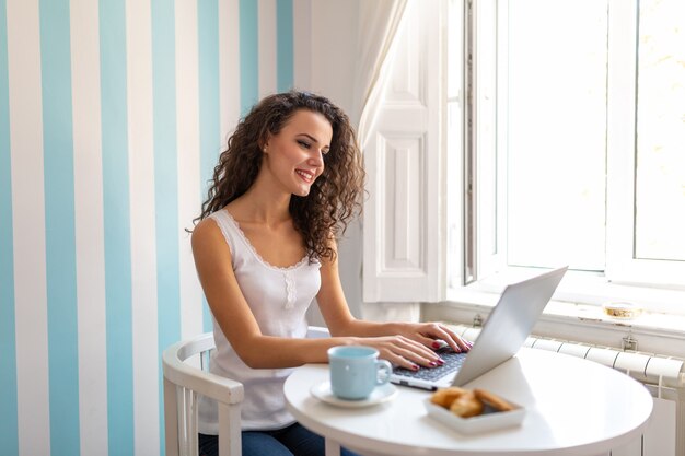 Gelukkige toevallige mooie succesvrouw die aan laptop thuis werkt