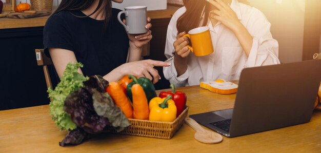 Foto gelukkige twee jonge vrouwen die laptopcomputer kijken tijdens het samen koken in de keukenruimte thuis twee jonge, diverse lesbische vrouwen die samen tijd doorbrengen lgbt en genderidentiteitsconcept