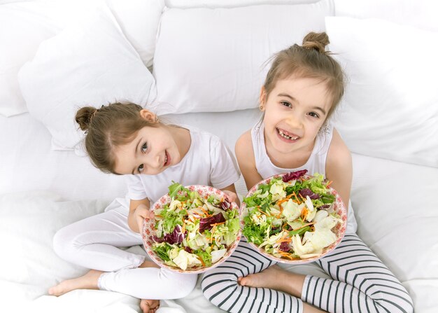 Gelukkige twee schattige kinderen groentesalade eten in de slaapkamer op het bed. Gezonde voeding voor kinderen en tieners.