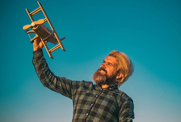 Gelukkige uitdrukking Gelukkige bebaarde man speelt met speelgoedvliegtuig Grappige gekke man met een houten vliegtuig Dromen van vliegen Reisconcept Start creativiteit opstarten