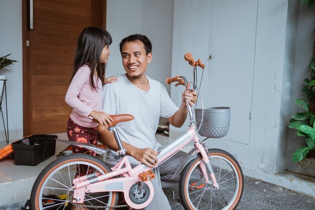 Gelukkige vader die een fiets vasthoudt en naar zijn dochter kijkt