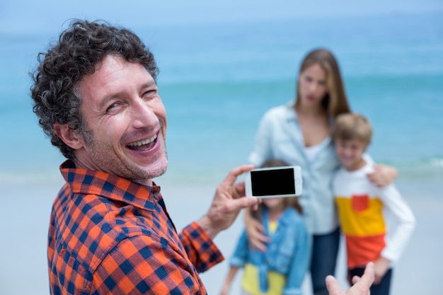 Gelukkige vader die familie met cellphone fotograferen bij strand