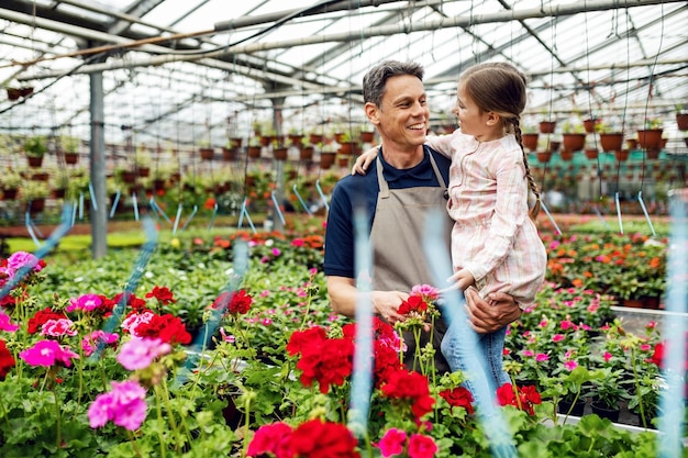 Foto gelukkige vader die met zijn dochter communiceert terwijl hij voor bloemen zorgt op de plantenkwekerij