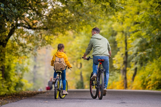 Gelukkige vader en dochter fietsen op zonnige dag in het herfstpark