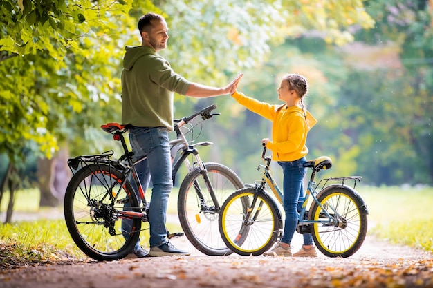 Gelukkige vader en dochter lopen op een zonnige dag met fietsen in het herfstpark