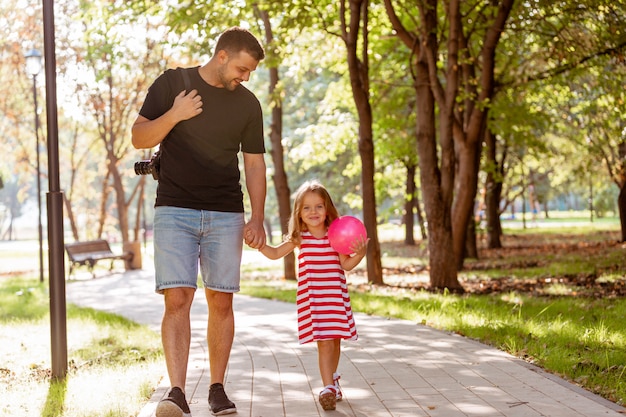 gelukkige vader en meisje lopen in de hand houden in het park van de zomer