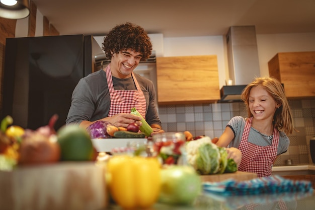 Gelukkige vader en zijn dochter genieten en hebben plezier in het samen maken en hebben van een gezonde maaltijd in hun thuiskeuken.