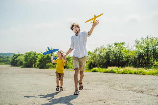 Gelukkige vader en zoon spelen met speelgoedvliegtuig tegen de achtergrond van de oude landingsbaan Reizen met kinderen concept