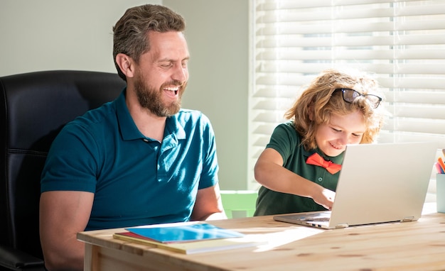 Gelukkige vader helpt zijn schoolzoon om thuis met laptop te studeren, webinar