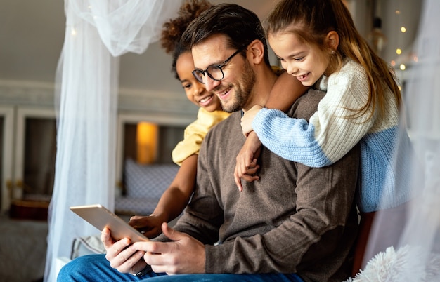 Gelukkige vader met multi-etnische dochters die thuis met digitale tablet spelen