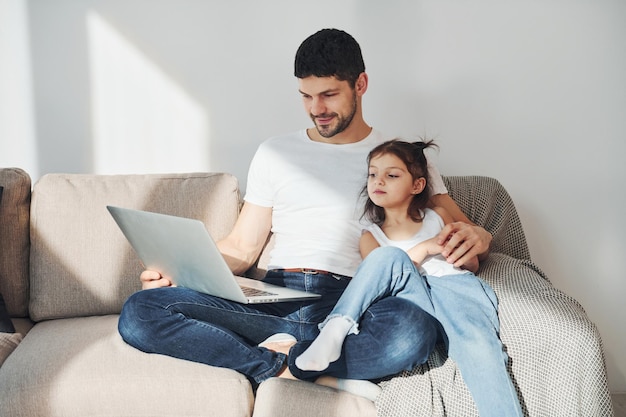Gelukkige vader met zijn dochter die samen thuis vrije tijd met laptop doorbrengt