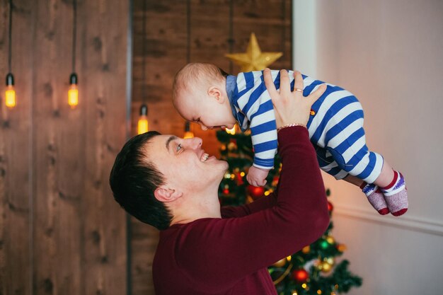 Gelukkige vader met zoontje in handen in de buurt van kerstboom Concept van vriendelijke familie Nieuwe jaartijd