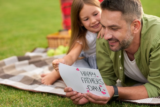 Gelukkige vader ontvangt handgemaakte ansichtkaart van zijn dochter, vader en zijn kleine meisje met een picknick