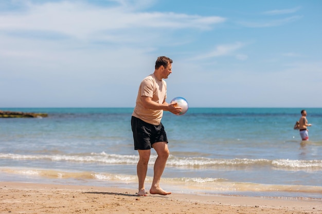 Gelukkige vader volwassen man op het strand speelt met een bal op het zand Reizen en vrije tijd