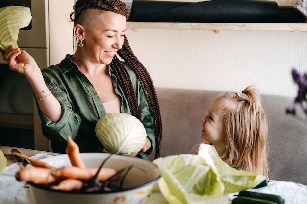 Gelukkige veganistische familiemoeder en babydochter die samen koken en plezier hebben in het koken van de familie in de keuken