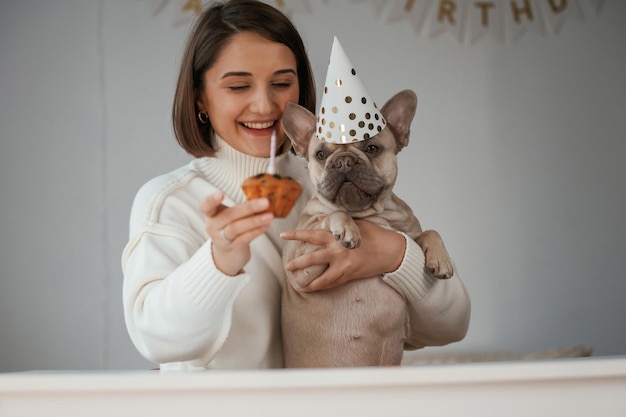 Gelukkige verjaardag huisdier in hoed en met taart jonge vrouw is met haar pug hond thuis