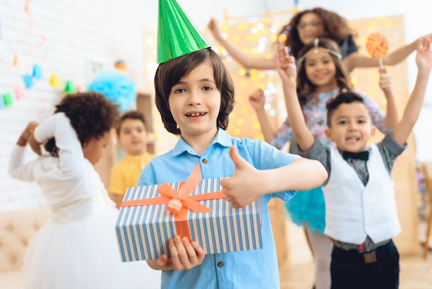 Gelukkige verjaardag jongen in groene feestelijke hoed laat zien dat hij blij is met cadeau.