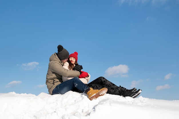 Gelukkige verliefde paar zit op sneeuw en omarmen. Blauwe lucht op de achtergrond.