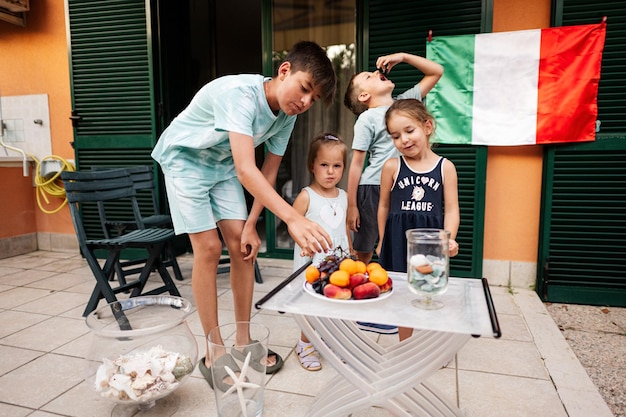 Gelukkige vier kinderen tegen de Italiaanse vlag vieren de Dag van de Republiek van Italië en eten fruit