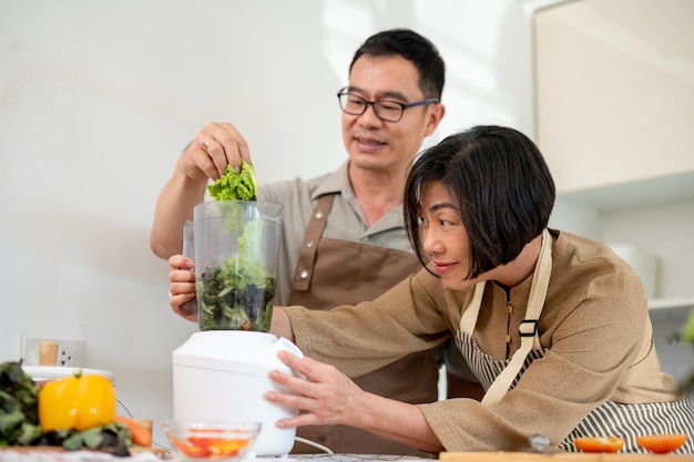 Gelukkige volwassen Aziatische paren maken gezonde groene smoothie in de keuken samen met behulp van een blender