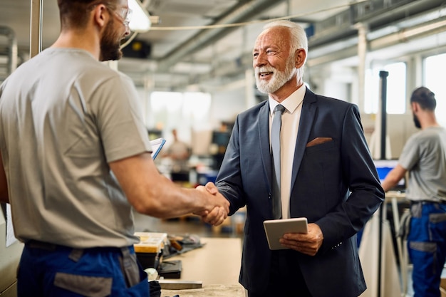 Gelukkige volwassen manager die een werknemer begroet tijdens een bezoek aan een industriële faciliteit