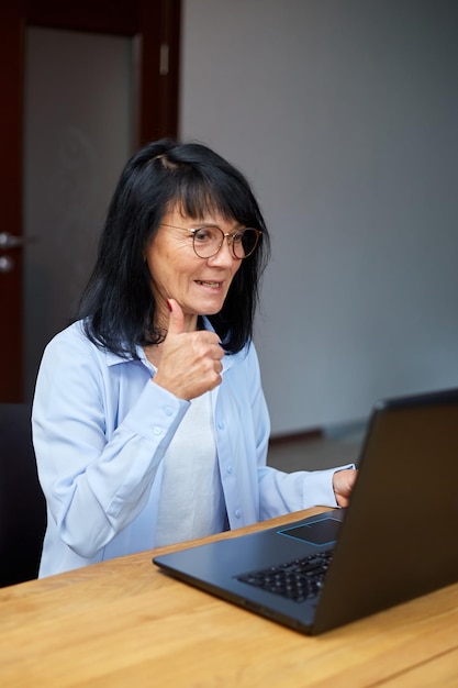 Gelukkige volwassen oudere vrouw zegt hallo tijdens conferentiegesprekken in videochatvergadering op laptop