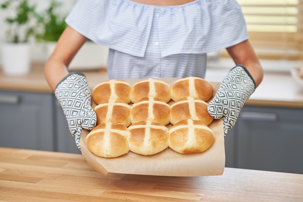 Gelukkige volwassen vrouw die warme kruisbroodjes klaarmaakt voor Pasen in de keuken