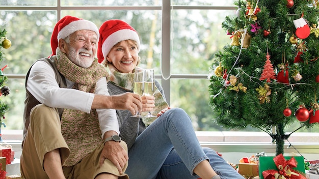 Gelukkige volwassen vrouw en oude man die het cadeau onderzoeken terwijl ze op een tapijt tussen versierde kerstbomen tegen het raam thuis zitten