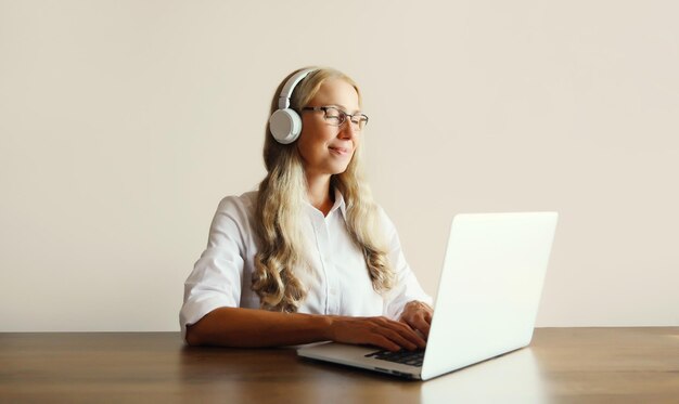 Gelukkige volwassen vrouw luistert naar muziek in koptelefoon werkt met laptop zit aan het bureau thuis