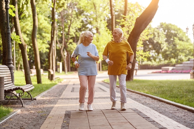 Gelukkige volwassen vrouw met echtgenoot rennen langs de weg in het pittoreske park