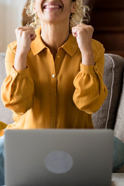 Foto gelukkige volwassen vrouw ontvangt melding op laptop computer en vieren met vreugde vrouwelijke mensen thuis genieten van online technologie verrast vrouw van middelbare leeftijd zit op de bank voor nieuws op pc notebook