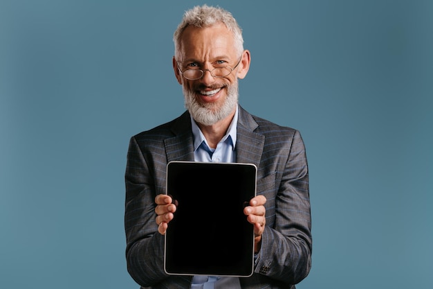 Gelukkige volwassen zakenman die het touchscreen van zijn digitale tablet tegen een gekleurde achtergrond toont