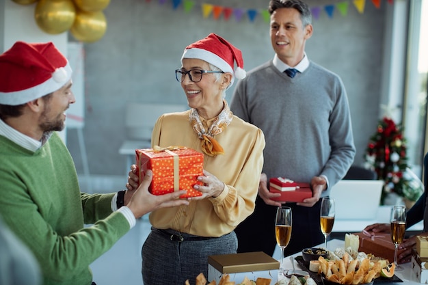 Gelukkige volwassen zakenvrouw die kerstcadeau ontvangt op kantoorfeest