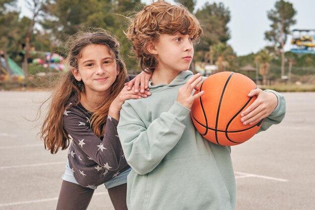 Foto gelukkige vriendelijke tiener jongen en meisje met basketbal staan op straat tijdens het weekend in de zomer